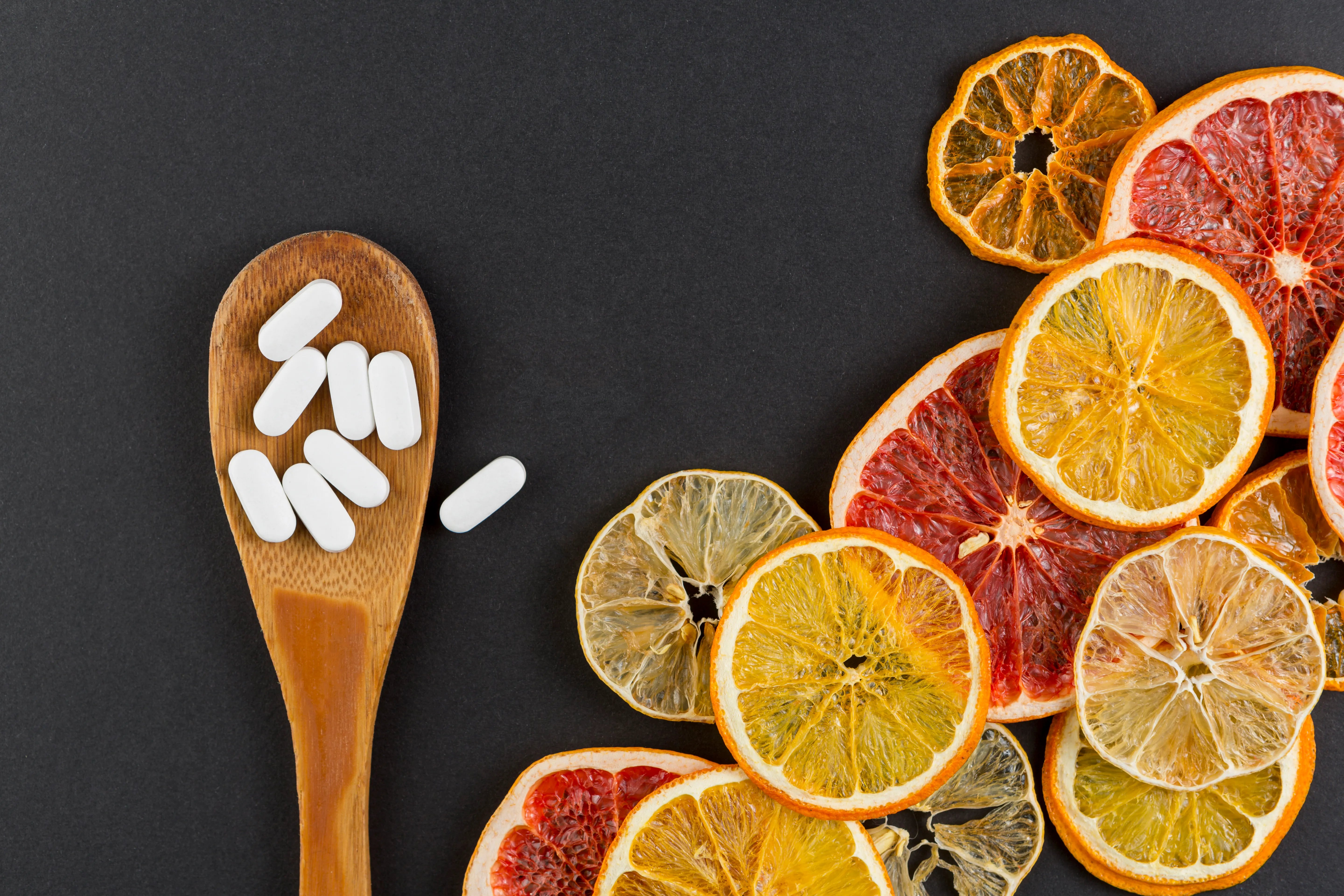Gélules blanches sur cuillère en bois avec tranches d’agrumes séchées dont orange sanguine Moro, illustrant le complément Morosil® 400 mg