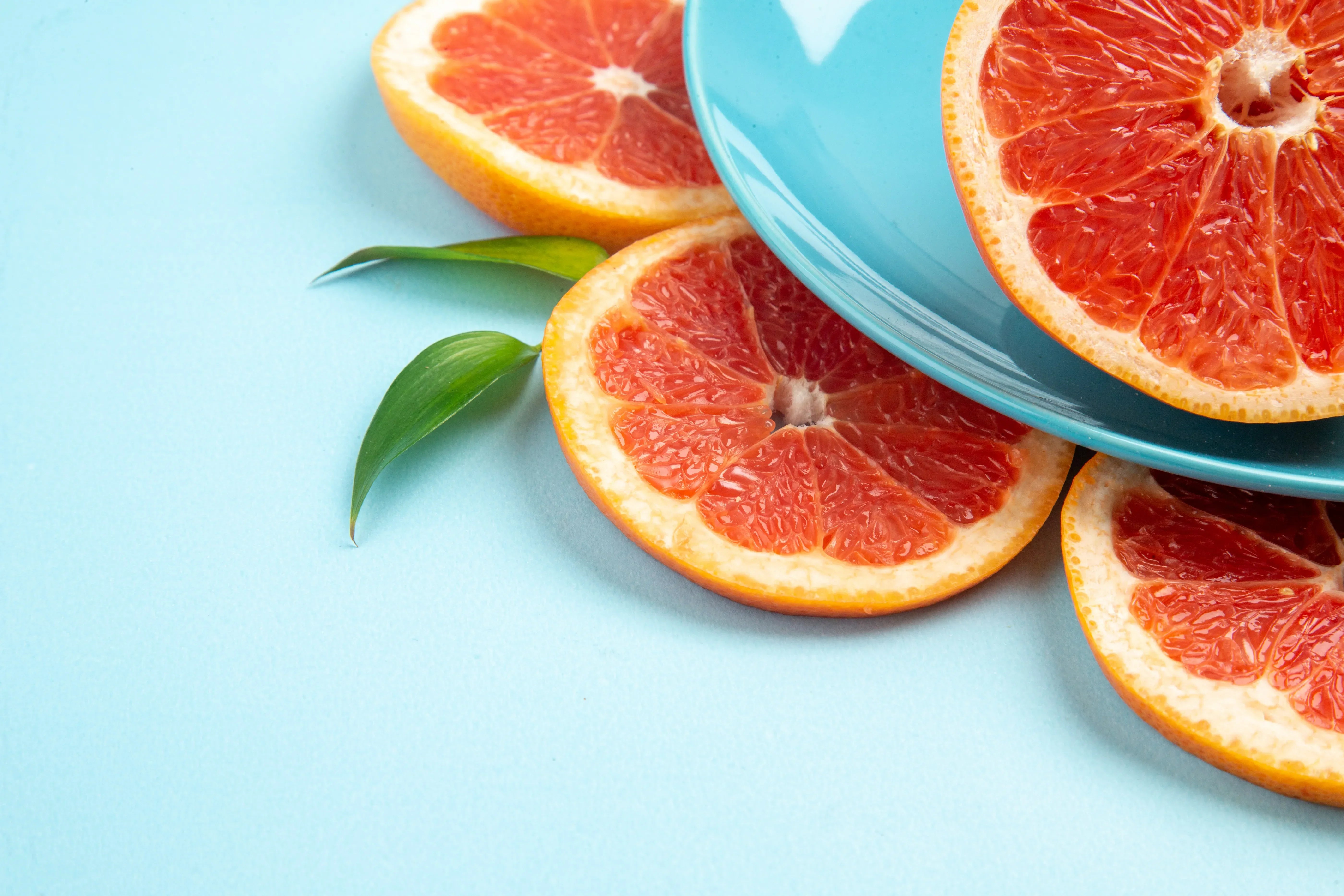 Tranches d’orange sanguine Moro disposées sur fond bleu clair avec feuilles vertes, illustrant l’ingrédient naturel du Morosil® 400